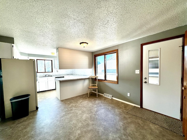 kitchen featuring white cabinets, a healthy amount of sunlight, white refrigerator, and kitchen peninsula