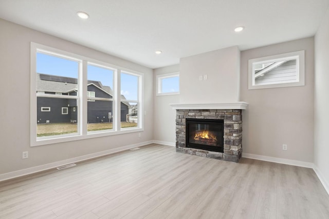 unfurnished living room with a stone fireplace and light hardwood / wood-style floors