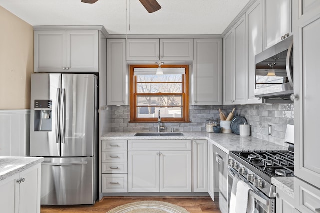 kitchen featuring sink, light hardwood / wood-style flooring, appliances with stainless steel finishes, gray cabinets, and light stone countertops