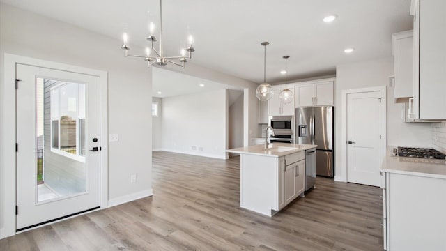 kitchen featuring white cabinetry, backsplash, a center island with sink, pendant lighting, and appliances with stainless steel finishes