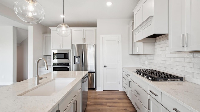 kitchen with light stone counters, hanging light fixtures, white cabinets, appliances with stainless steel finishes, and sink