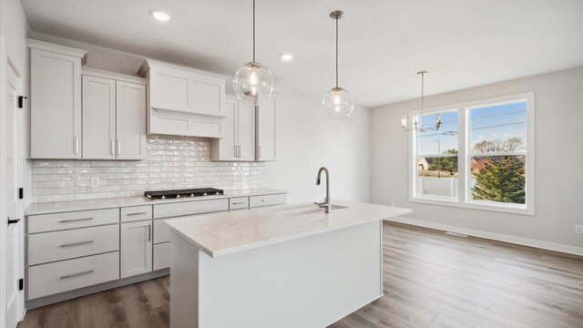 kitchen featuring light stone counters, pendant lighting, an island with sink, white cabinetry, and sink