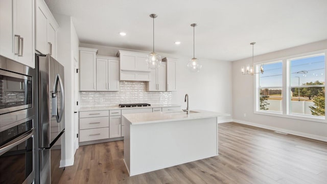 kitchen featuring stainless steel appliances, an island with sink, hanging light fixtures, sink, and white cabinetry