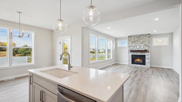 kitchen featuring sink, light stone counters, stainless steel dishwasher, a center island with sink, and a stone fireplace