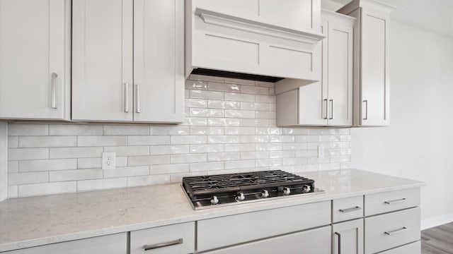10238 Arrowwood Path, Woodbury, MN 55129 - kitchen featuring stainless steel gas cooktop, light stone countertops, tasteful backsplash, white cabinetry, and premium range hood