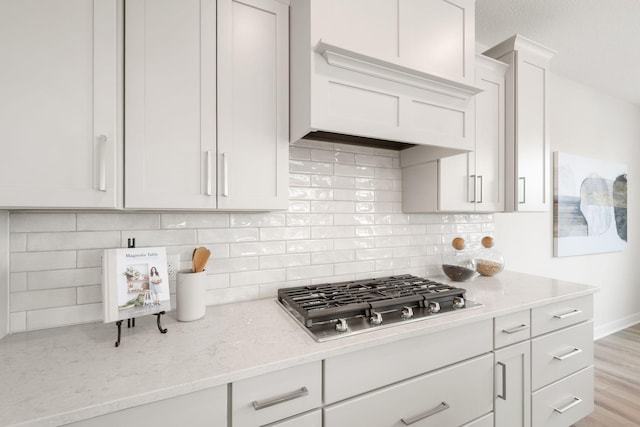 10238 Arrowwood Path, Woodbury, MN 55129 - kitchen featuring stainless steel gas cooktop, light stone counters, custom range hood, white cabinetry, and decorative backsplash