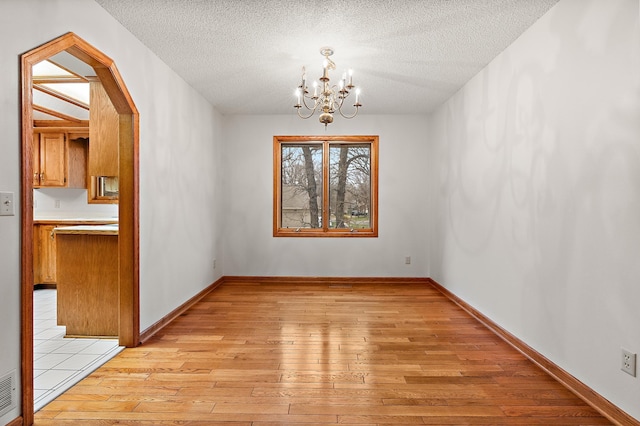 unfurnished dining area with a notable chandelier, light hardwood / wood-style floors, and a textured ceiling