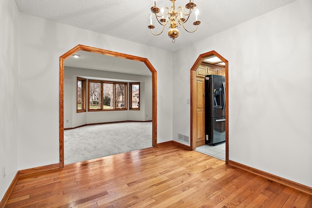 spare room featuring light hardwood / wood-style flooring, a textured ceiling, and a notable chandelier