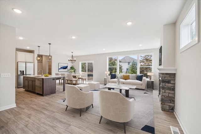 living room featuring a stone fireplace, light hardwood / wood-style flooring, a notable chandelier, and sink