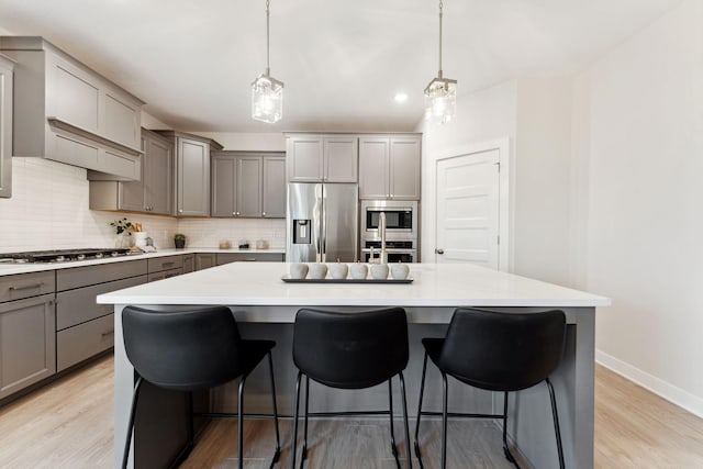 11728 35th St N, Lake Elmo, MN 55042 - kitchen with gray cabinetry, stainless steel appliances, baseboards, decorative backsplash, and a kitchen breakfast bar
