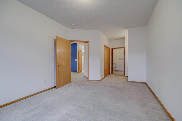 unfurnished bedroom with ensuite bath, a textured ceiling, light carpet, and a closet