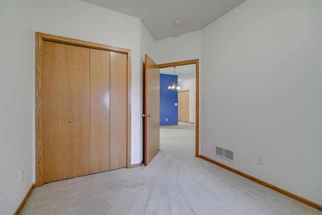 unfurnished bedroom featuring light carpet, a chandelier, and a closet