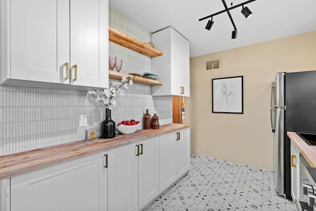 kitchen with backsplash, white cabinets, stainless steel refrigerator, and wood counters