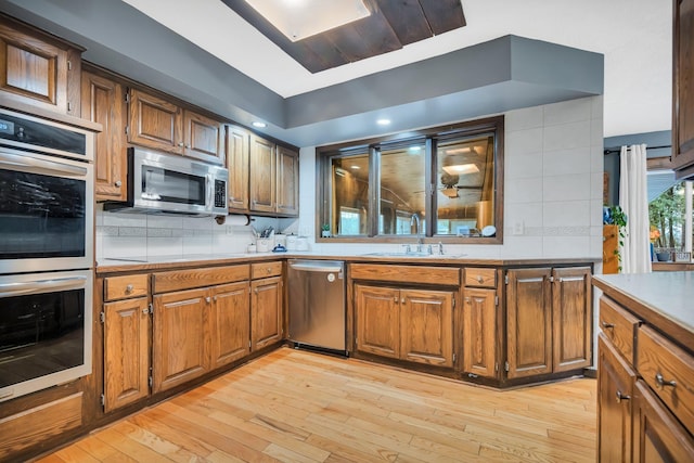 kitchen with decorative backsplash, appliances with stainless steel finishes, light wood-type flooring, and sink