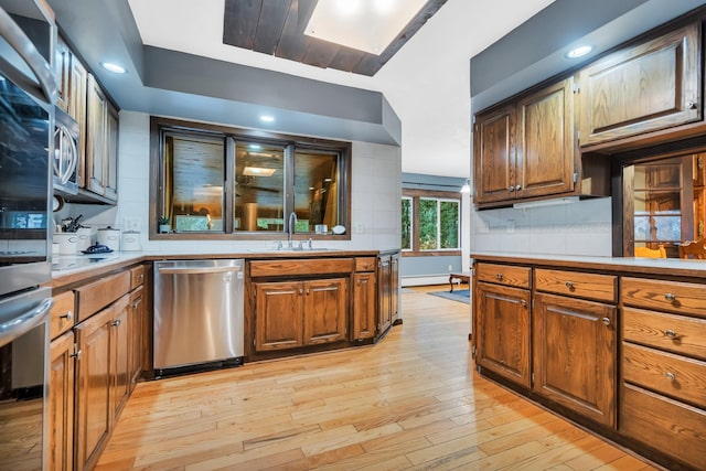 kitchen with backsplash, stainless steel appliances, sink, a baseboard radiator, and light hardwood / wood-style floors