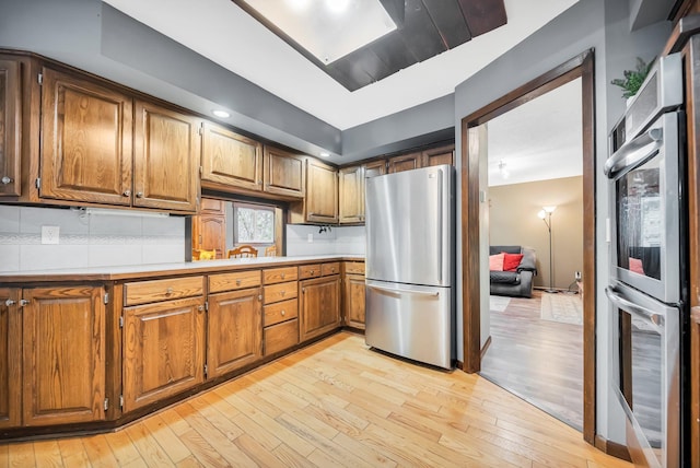 kitchen with appliances with stainless steel finishes, light hardwood / wood-style floors, and tasteful backsplash