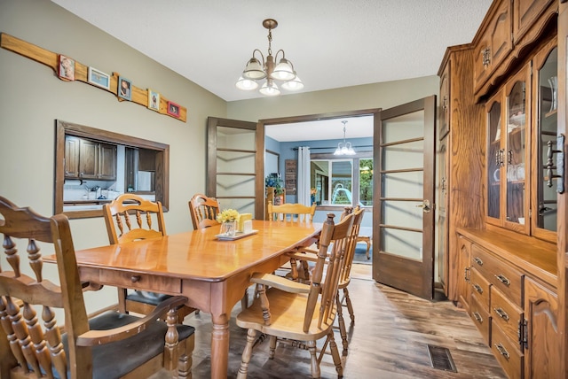 dining area with french doors, a textured ceiling, hardwood / wood-style flooring, and a notable chandelier