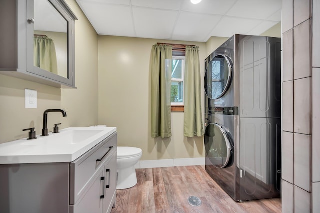 bathroom with wood-type flooring, stacked washer / drying machine, toilet, a paneled ceiling, and vanity