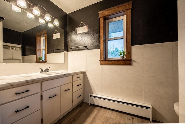 bathroom with vanity, a textured ceiling, baseboard heating, hardwood / wood-style flooring, and tile walls