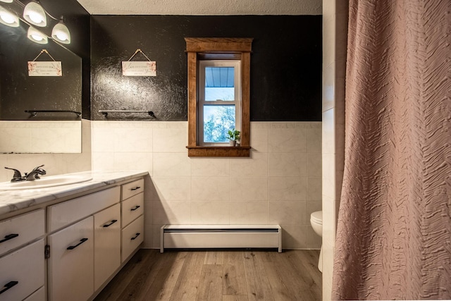 bathroom with hardwood / wood-style flooring, vanity, toilet, tile walls, and a baseboard heating unit