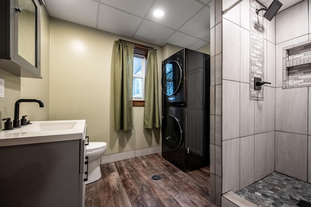 bathroom with a drop ceiling, hardwood / wood-style floors, stacked washer / drying machine, toilet, and vanity