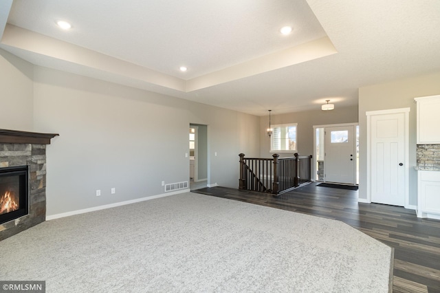 unfurnished living room featuring a tray ceiling, a fireplace, and dark hardwood / wood-style flooring