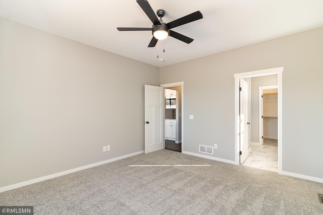 unfurnished bedroom featuring a walk in closet, light colored carpet, a closet, and ceiling fan