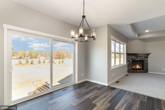 unfurnished dining area featuring dark wood-style flooring, a stone fireplace, visible vents, baseboards, and a chandelier