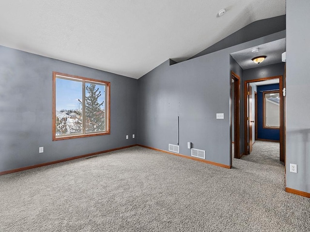 empty room featuring vaulted ceiling, carpet, visible vents, and baseboards