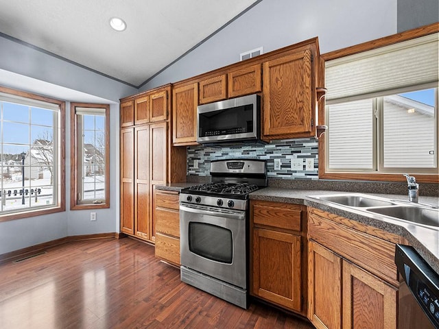 kitchen featuring brown cabinets, visible vents, appliances with stainless steel finishes, vaulted ceiling, and a sink