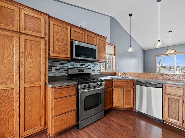 kitchen featuring appliances with stainless steel finishes, brown cabinets, dark wood-style flooring, vaulted ceiling, and a sink