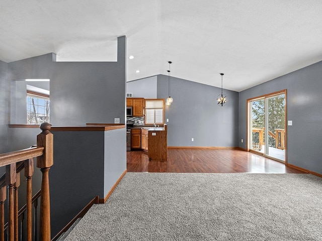 interior space featuring lofted ceiling, stainless steel appliances, a healthy amount of sunlight, dark colored carpet, and brown cabinetry