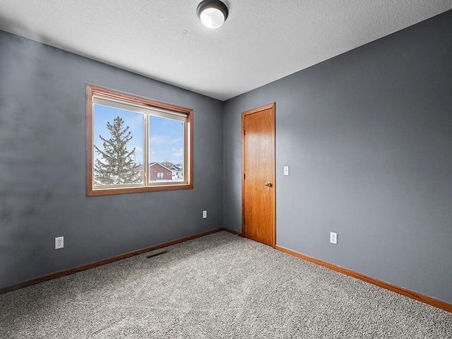 carpeted spare room with a textured ceiling, visible vents, and baseboards