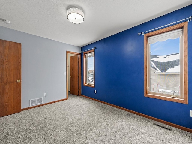 empty room with baseboards, a textured ceiling, visible vents, and carpet flooring