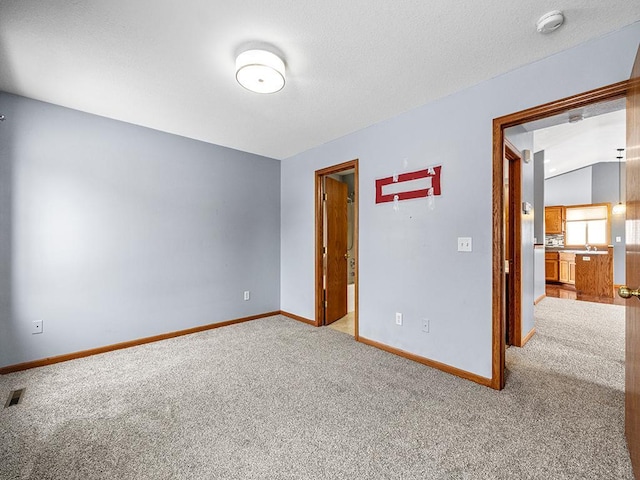 carpeted empty room featuring visible vents, vaulted ceiling, a textured ceiling, and baseboards