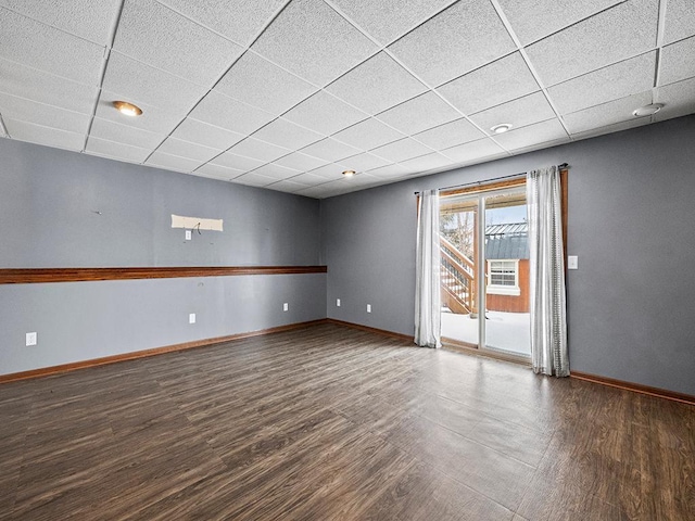 spare room with a paneled ceiling, baseboards, and wood finished floors