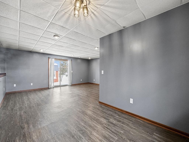 spare room with wood finished floors, a paneled ceiling, and baseboards