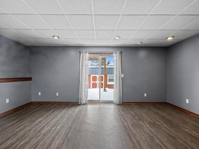 empty room with wood finished floors, a paneled ceiling, and baseboards