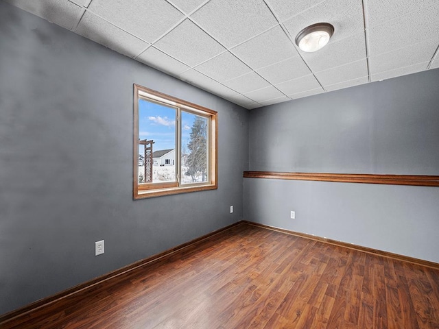 spare room with a drop ceiling, wood finished floors, and baseboards