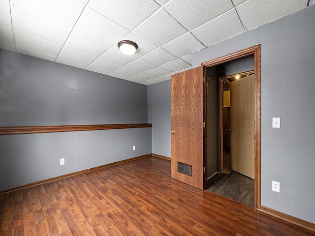 unfurnished room with baseboards, visible vents, a drop ceiling, and wood finished floors