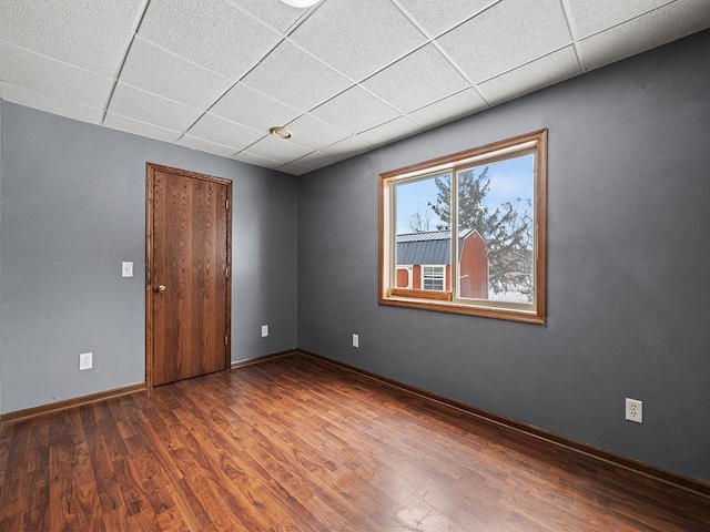 spare room with baseboards, a drop ceiling, and wood finished floors