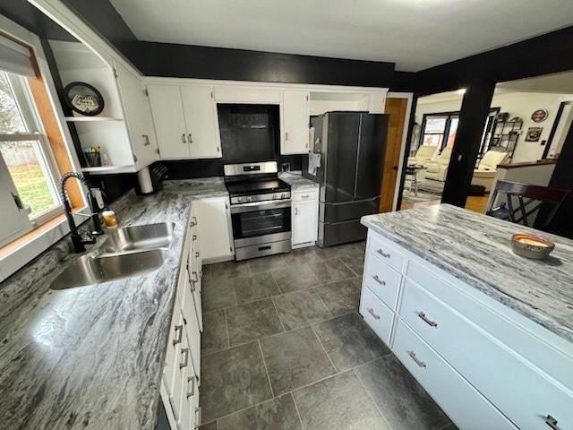 kitchen with black refrigerator, sink, stainless steel range, light stone countertops, and white cabinetry