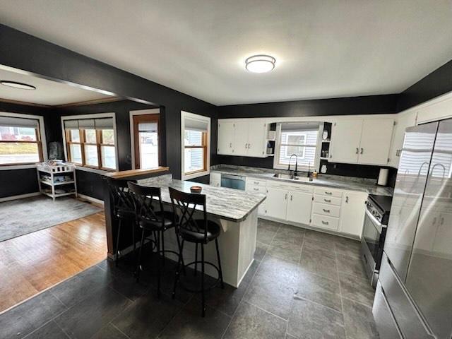 kitchen with sink, appliances with stainless steel finishes, a kitchen bar, white cabinets, and dark wood-type flooring