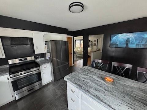 kitchen with black fridge, stainless steel stove, light stone counters, and white cabinets