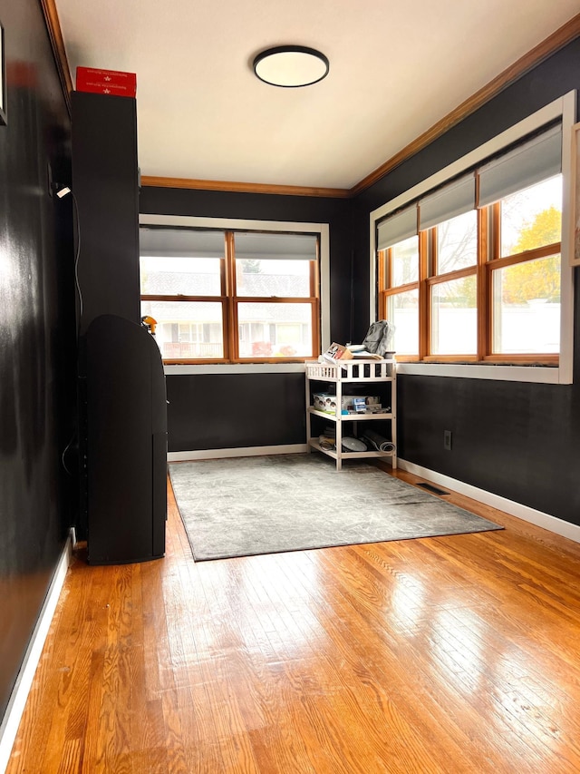 unfurnished bedroom featuring multiple windows, wood-type flooring, built in desk, and ornamental molding