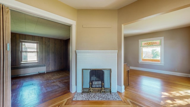 unfurnished living room with a fireplace, plenty of natural light, wood walls, and radiator