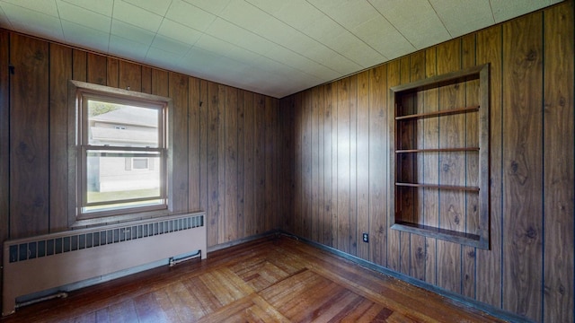 spare room featuring radiator, wood-type flooring, and wood walls