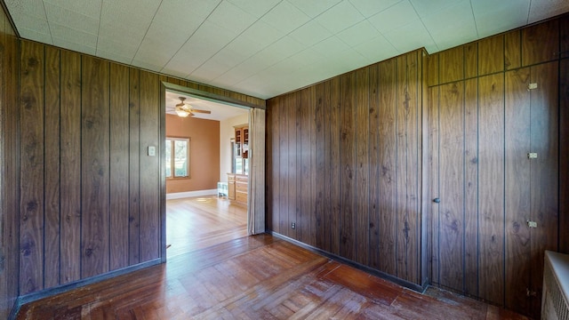 empty room with wood walls, dark parquet floors, and ceiling fan