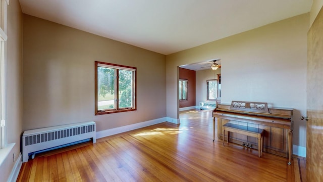 unfurnished room with light wood-type flooring, radiator heating unit, and ceiling fan