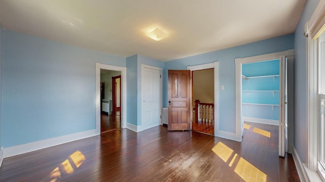 unfurnished bedroom with dark wood-type flooring, radiator heating unit, and a closet